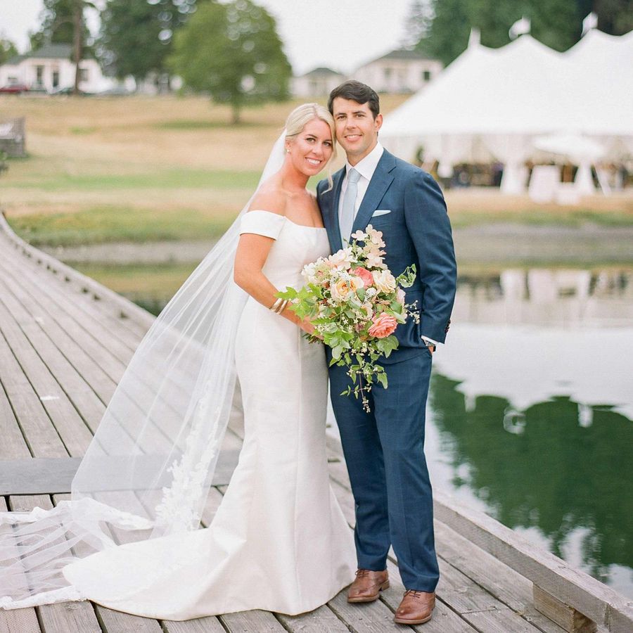 Bride in an off-the-shoulder gown with bouquet and veil and groom in navy suit on a dock in the San Juan Islands