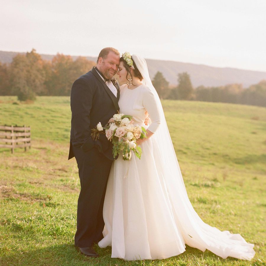 Groom in tuxedo and bride in long sleeve gown with floral headband and veil pose at a Shenandoah Valley farm